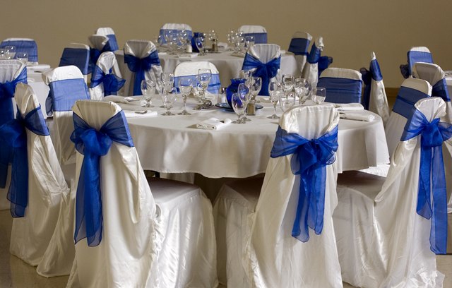Blue tulle bows are tied around white fabric draped over chairs at a ...