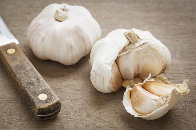 Fresh garlic with large knife on cutting board.