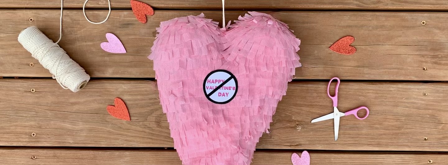 Broken-heart piñata surrounded by art supplies against a wood background