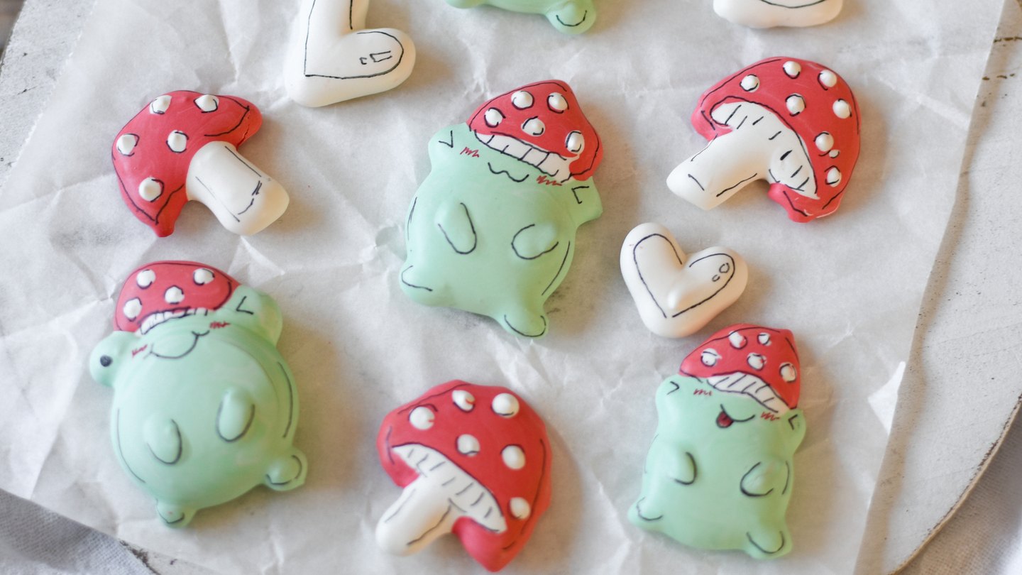 Meringue cookies shaped like green frogs and red and white mushrooms