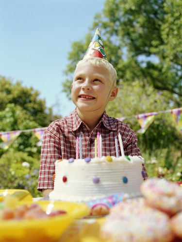Boy (6-8) sitting outdoors by birthday cake, smiling