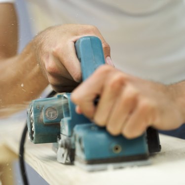close-up of a person's hand using an electric sander on a piece of wood