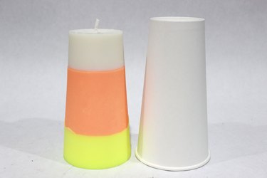 A striped DIY candy corn candle set next to a paper cup mold