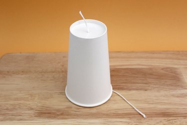 A white paper cup upside down on a tape with a candle wick threaded through its base
