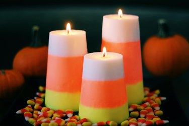 candy corn candles on a black table with candy corn and small pumpkins around them