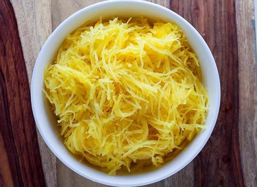 Overhead view of a white bowl on a rustic wooden table, filled with long noodle-like threads of spaghetti squash