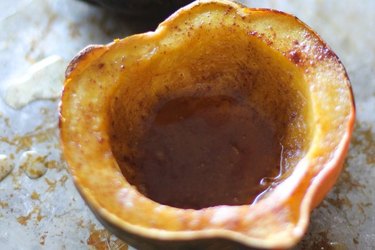 An overhead view of a halved, baked acorn squash with spices and syrup in the cavity