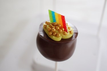 Chocolate cauldron cake pop garnish with yellow icing, rainbow candy and gold candy pearls