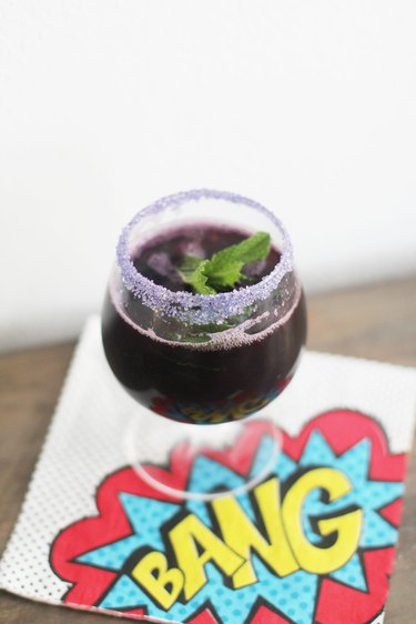 Glass of punch rimmed with purple sugar and garnished with mint
