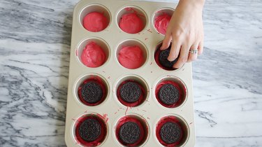 Placing Oreos on top of red chocolate in muffin tin
