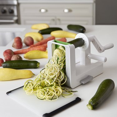 OXO spiralizer on white countertop, with vegetables waiting to be sliced.