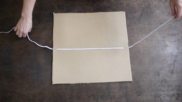 Pulling elastic string through slits in cardboard