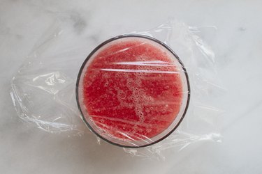 A bowl of pureed watermelon sorbet covered with plastic wrap to freeze for watermelon sorbet