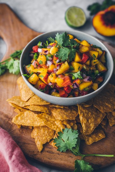 Bowl of peach salsa on a wood board with chips