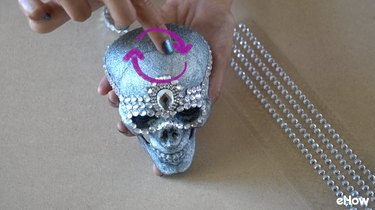 Applying gemstone strips to plastic skull for DIY Gemstone Studded Halloween Skull