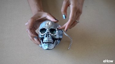 Applying gemstone strip around eyes of plastic skull for DIY Gemstone Studded Halloween Skull