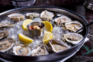 Fresh raw oysters with lemons on ice in metal tray