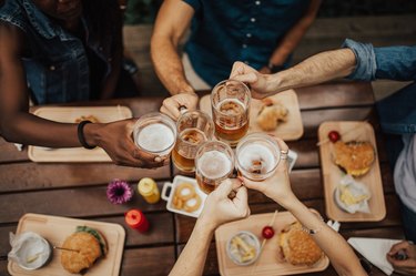 Five hands clinking beer mugs and glasses over pub food