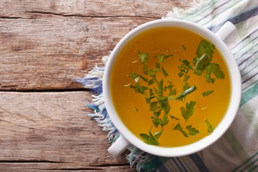 meat broth with parsley in bowl closeup. horizontal top view