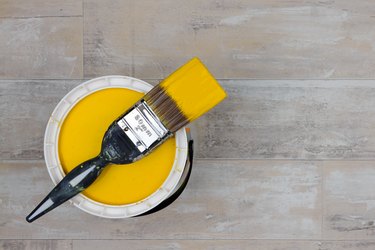 Loaded paintbrush across an open can of bright yellow paint