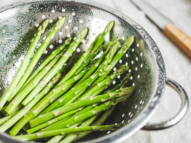 Washed asparagus in a metal colander on a kitchen table. Preparation vegetarian healthy food.