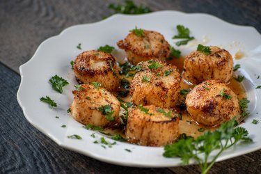 sea scallops on white plate with green herbs