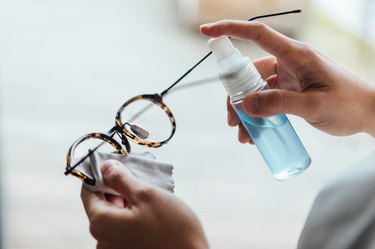 Close up shot of woman cleaning eyewear surface with sanitising spray