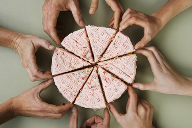 Group of eight people reaching for slice of cake, close-up, overhead view