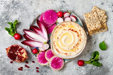 Homemade hummus seasoned with olive oil and paprika and fresh vegetables: radishes, watermelon radish, red chicory, pomegranate. Healthy vegetarian appetizer or snack platter