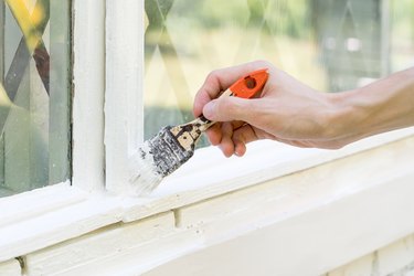 A Man Paints An Old Wooden Window With White Paint