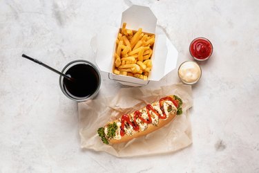 Tasty hot dog with sauces, french fries and drink on light table