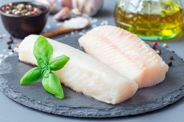 Fresh raw cod fillet with spices, pepper, salt, basil on stone plate, horizontal