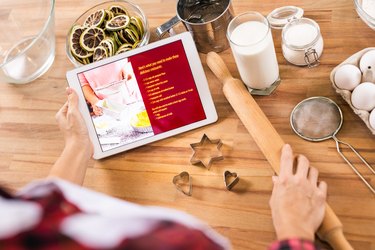 Woman holding touchpad with recipe and rolling-pin before making cookies at home