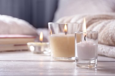 Home interior. Still life with detailes. Several candles on white wooden table in front of bed, the concept of cosiness.