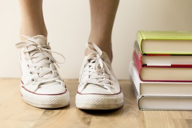 White sneakers and stack of books on the floor. Student, education and knowledge concept