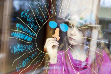 Girl painting sun on windowpane