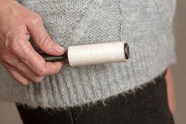 Woman's hand holding a adhesive roller brush to collect hair and fluff from a sweater