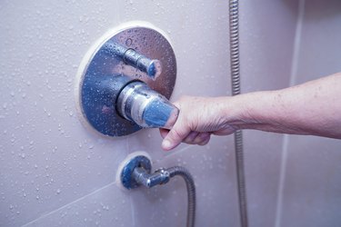 Cropped Hand Of Woman Holding Handle Of Faucet On Wall In Bathroom