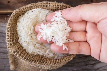 Woman's hand picking uncooked rice in a small  burlap sack.