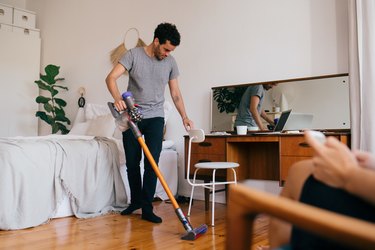 Full length of man cleaning bedroom with vacuum cleaner