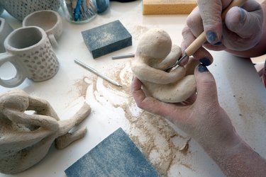 Hands of female artist scraping the dried clay sculpture