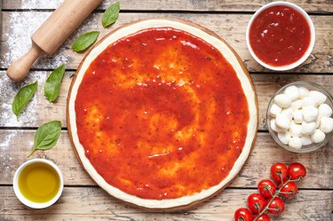 Raw dough for pizza with ingredient: tomato sauce, mozzarella, tomatoes, basil, olive oil, cheese, spices served on rustic wooden table. Flat lay. Italian pizza margarita