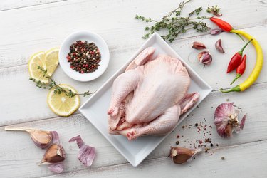 Pollo, hierbas y especias crudas en fondo de madera blanco