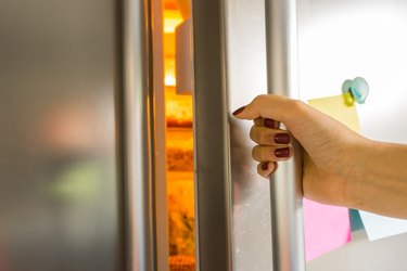 Woman hand opens refrigerator door