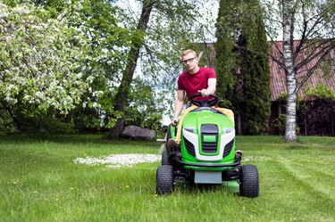 Young Man Riding Lawn Mower At Grassy Field