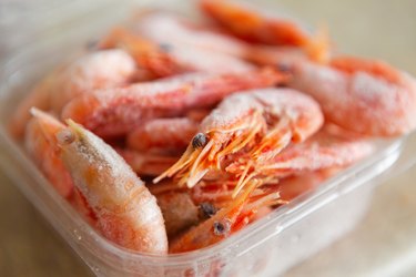 Frozen shrimps in plastic container box on kitchen table for cooking.