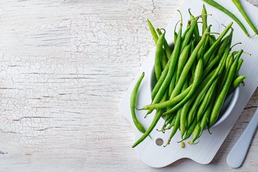 Green beans in white bowl on cutting board. Top view. Copy space