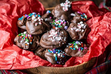 A bowl of chocolate candy coated with sprinkles and crushed peppermints atop red tissue paper.