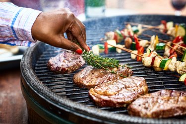 Woman basting meat on barbecue with fresh herbs