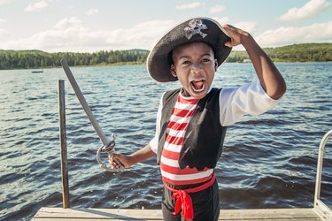 Very expressive african-american child dressed as pirate on a lake.